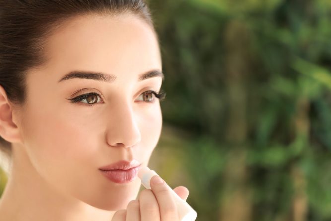 Beautiful young woman applying chapstick onto lips at home