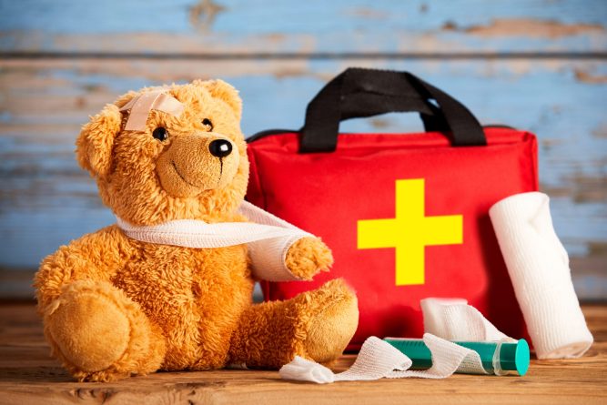 Paediatric healthcare concept with a little teddy bear with its arm in a sling alongside a first aid kit and bandages on rustic wood