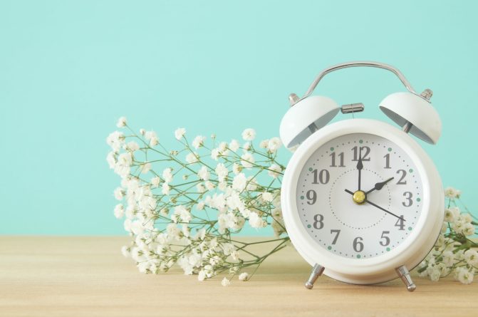 Image of spring Time Change. Summer back concept. Vintage alarm Clock over wooden table