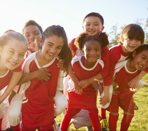 Kids in elementary school sports team piggybacking outdoors