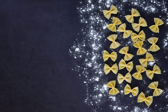 Appetizing pasta with your own hands - a lot of butterflies on a dark background, sprinkled with light wheat flour