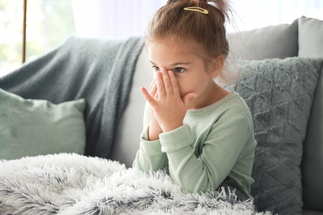 Sick little girl sitting on sofa at home