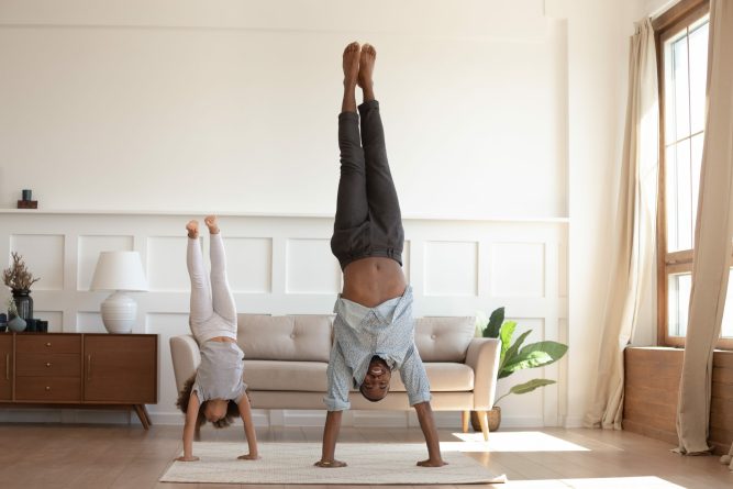 Full-length image african father and little daughter having fun fool around at home sportive active kid girl and dad do handstand position. Funny leisure activities, sporty healthy lifestyle concept