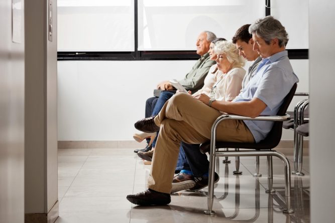 Row of multiethnic people sitting side by side while waiting for doctor in hospital lobby