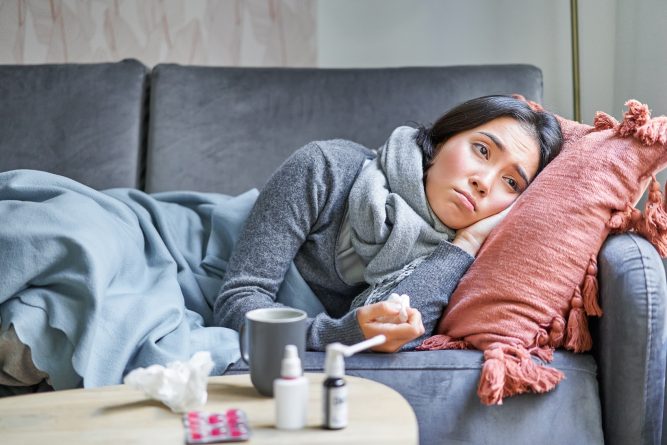 Sick sad korean woman lying on sofa, feeling unwell, catching cold, flu and temperature, looking upset, taking medication.